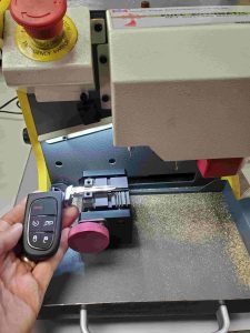 An automotive locksmith is cutting a new Dodge key fob